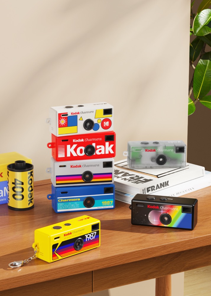 Kodak Charmera keychain digital cameras in seven retro blind-box designs displayed with a roll of Kodak film on a wooden desk